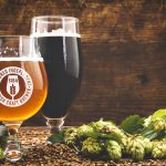 beer surrounded by hops on wooden background